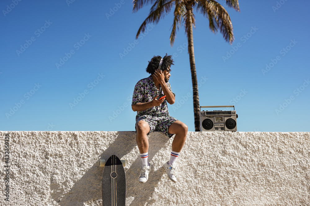 Fototapeta premium Young trendy african man enjoy music playlist in summer vaction in the city - Skater boy with retro boombox outdoor