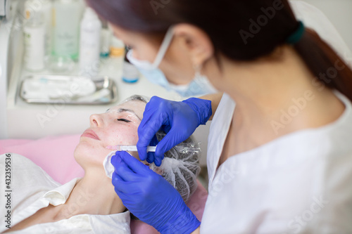 Beautiful woman at the dermatology clinic. Cosmetologist doing injections on the face and mouth area of female client. Skin biorevitalizing and anti-aging therapy