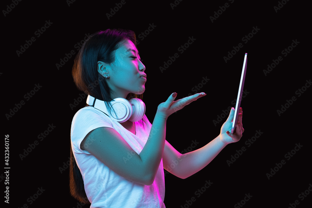 Obraz premium Asian young woman's portrait on dark studio background in neon. Concept of human emotions, facial expression, youth, sales, ad.