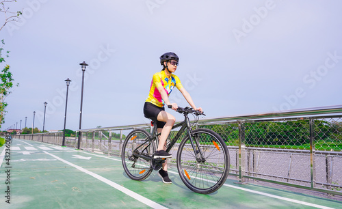 Young Asian healthy cyclist girl wearing helmet cycling and yellow shirt riding bike on bicycle path in the evening, healthy lifestyle concept.