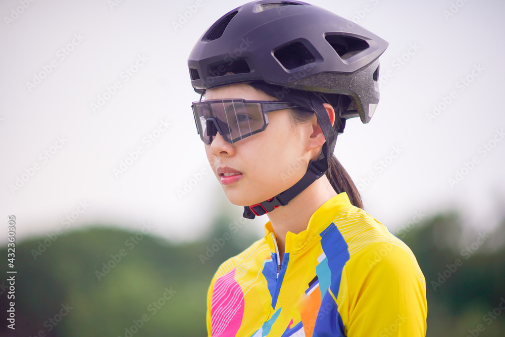 close up image of Young Asian cyclist girl wearing helmet cycling and yellow cycling shirt.