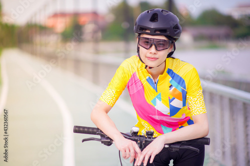 Portrait image of Young Asian cyclist girl wearing helmet cycling and yellow shirt riding bike, healthy lifestyle concept. © pangoasis