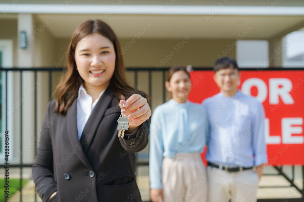 Asian real estate agent or realtor woman smiling and holding red file with showing house key with happy Asian couple hugging in front of thier house. Asian real estate agent or realtor woman smiling and holding red file with showing house key with happy Asian couple hugging in front of thier house.