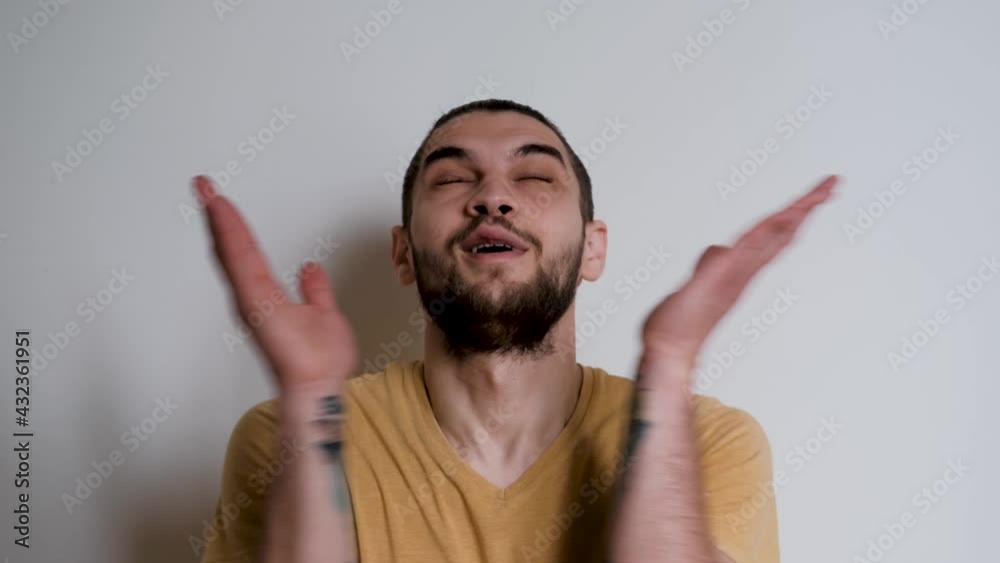 Human in yellow Tshirt on white studio background depicts emotions. Handsome Caucasian man with beard and ponytail on his head looks forward carefully, then looks up in surprise and blinks.