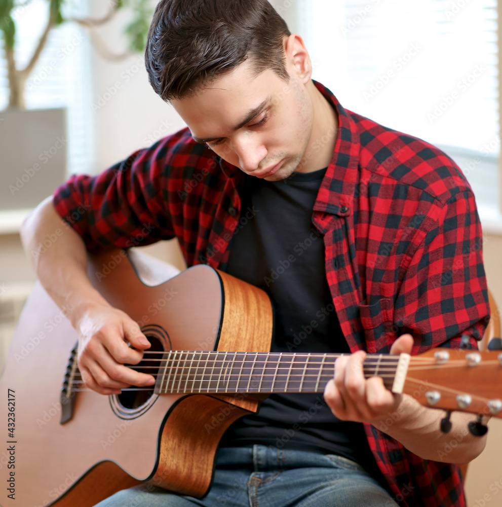 A young man learns to play the guitar using the Internet, laptop, online lesson. Hobby and leisure concept