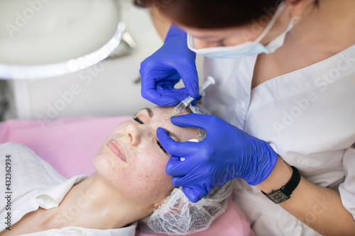 Cosmetology skin care. Doctor cosmetologist makes rejuvenating facial injections for tightening and smoothing wrinkles on the forehead of beautiful, young woman photo