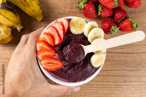 Açai, man holding an Brazilian frozen açai berry ice cream bowl. with fruits on wooden background. Summer menu front view