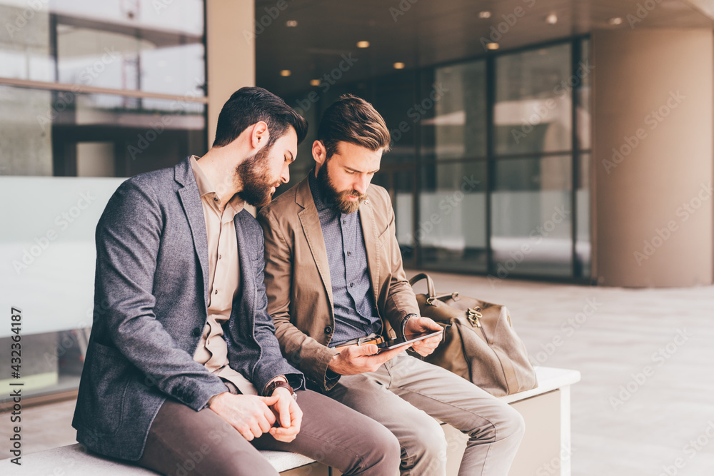 Two casual designer using tablet sitting outdoor Two casual designer using tablet sitting outdoor