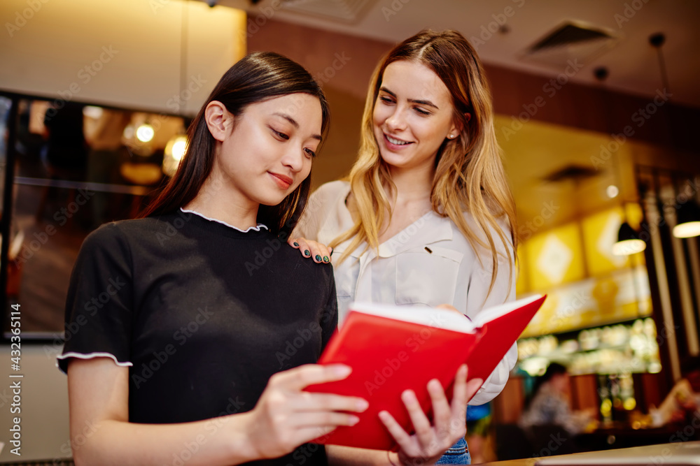 Young cheerful diverse women reading information in notebook and smiling Young cheerful diverse women reading information in notebook and smiling