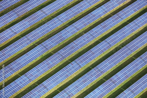 An aerial view taken from a helicopter of a solar power farm in Britain. The eco friendly and renewable photovoltaic panels make a repeating striped pattern of green grass and blue.