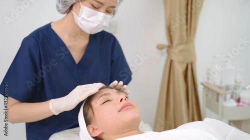 Beautician is doing cure procedures on client face in cosmetology clinic. Face of smiling woman closeup. Cosmetologist doctor is making myoplastic anti-aging facial massage to woman in beauty clinic.
