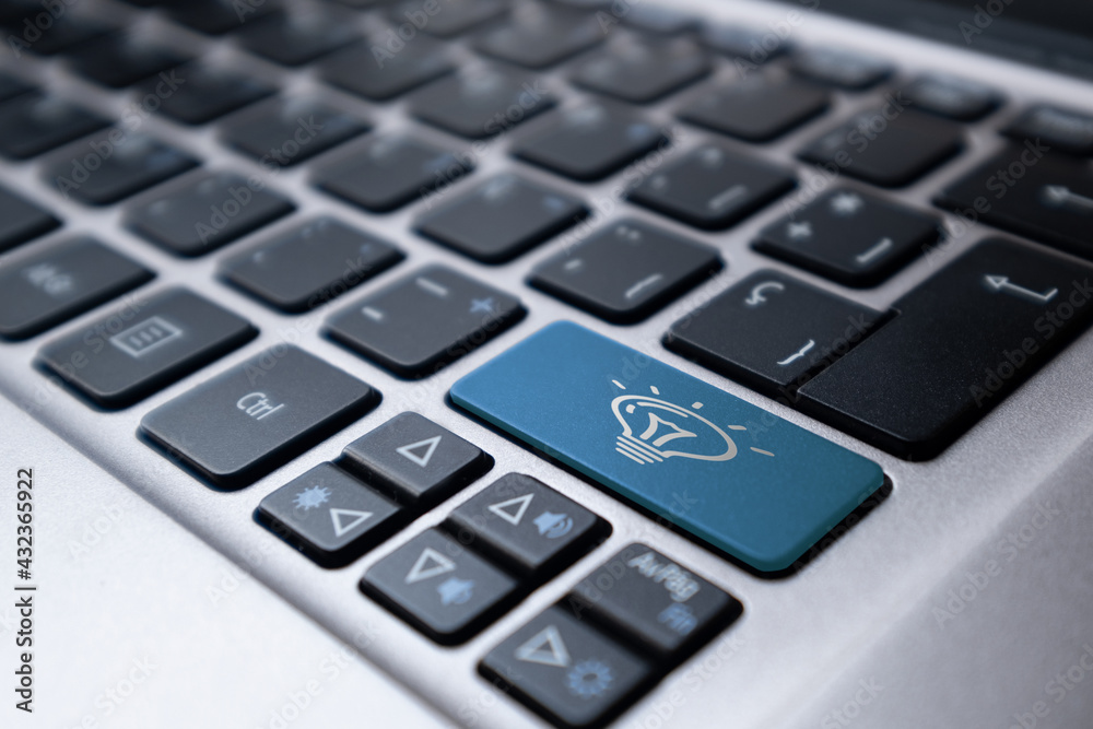 Laptop keyboard with a blue key with an idea symbol represented by a lit light bulb. Concept of idea, eureka, invention, online Laptop keyboard with a blue key with an idea symbol represented by a lit light bulb. Concept of idea, eureka, invention, online