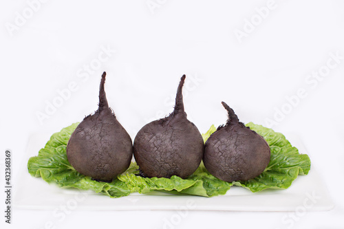 three whole organic unpeeled baked beetroots green lettuce leaves on white plate. healthy nutrition, vegetarian, vegetables diet, minimalistic lifestyle concept. copy space. isolated