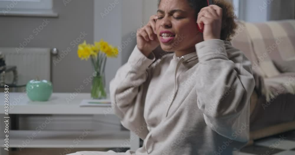 Middle shot of joyful African American woman enjoying music in headphones dancing indoors. Side view of cheerful funny young millennial resting at home on weekend. Cinema 4k ProRes HQ Middle shot of joyful African American woman enjoying music in headphones dancing indoors. Side view of cheerful funny young millennial resting at home on weekend. Cinema 4k ProRes HQ