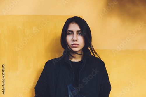 Quadro su tela Young woman in black clothes near yellow wall on street
