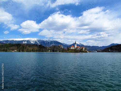 View of the church on the island on lake Bled and Bled castle and snow covered peaks of Karavanke mountains with mountain Stol behind in Gorenjska, Slovenia