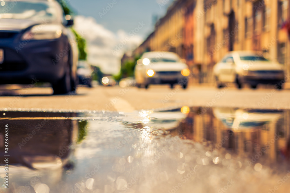 Sunny day after the rain in the city, the headlights of the approaching car. Close up view from the level of the puddle on the pavement