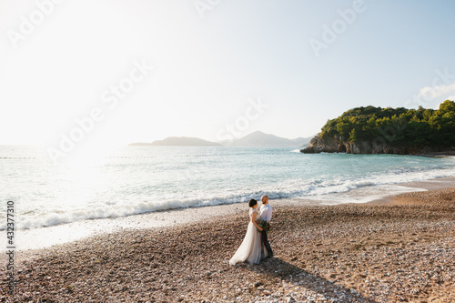 The bride and groom are hugging each other on the pebble beach by the sea 