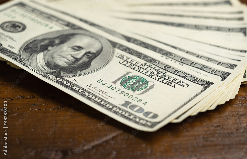 A money pile of fan stacked one hundred US banknotes with president Franklin portrait over wooden table background. Cash of hundred dollar bills, paper money currency. A money pile of fan stacked one hundred US banknotes with president Franklin portrait over wooden table background. Cash of hundred dollar bills, paper money currency.