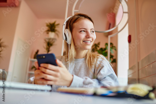 Happy Caucasian blogger in electronic headphones for noise cancellation enjoying music podcast from modern smartphone device, cheerful hipster girl in earphones listening positive audio records