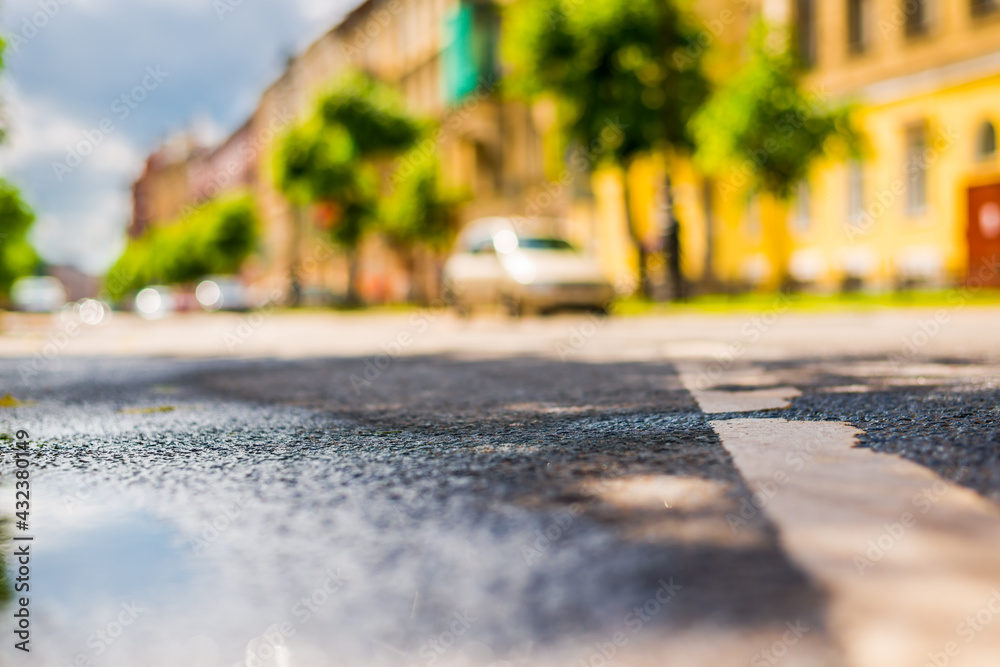 Sunny day after rain in the city, parked in the street car. Close up view from the puddle level near the dividing line on the asphalt Sunny day after rain in the city, parked in the street car. Close up view from the puddle level near the dividing line on the asphalt