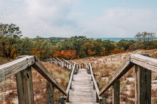 Fototapeta Naklejka Na Ścianę i Meble -  Wooden boardwalk stairs laid over the grassy sand dunes leading down into the colorful autumn forest, hiking around Lake Michigan at Indiana Dunes National Park, Indiana, USA.
