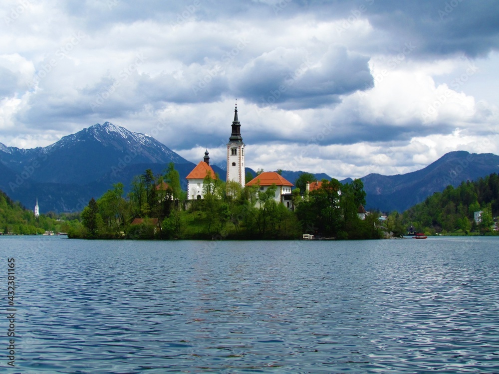 View of Bled lake and the island with the Pilgrimage church of the Assumption of Maria and Bled castle behind with snow covered peaks of Karavanke mountains