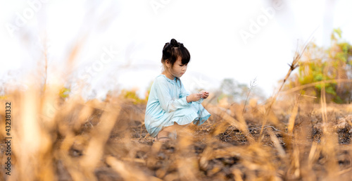 Cute little girl sitting on the grass in the forest behind the burning grass