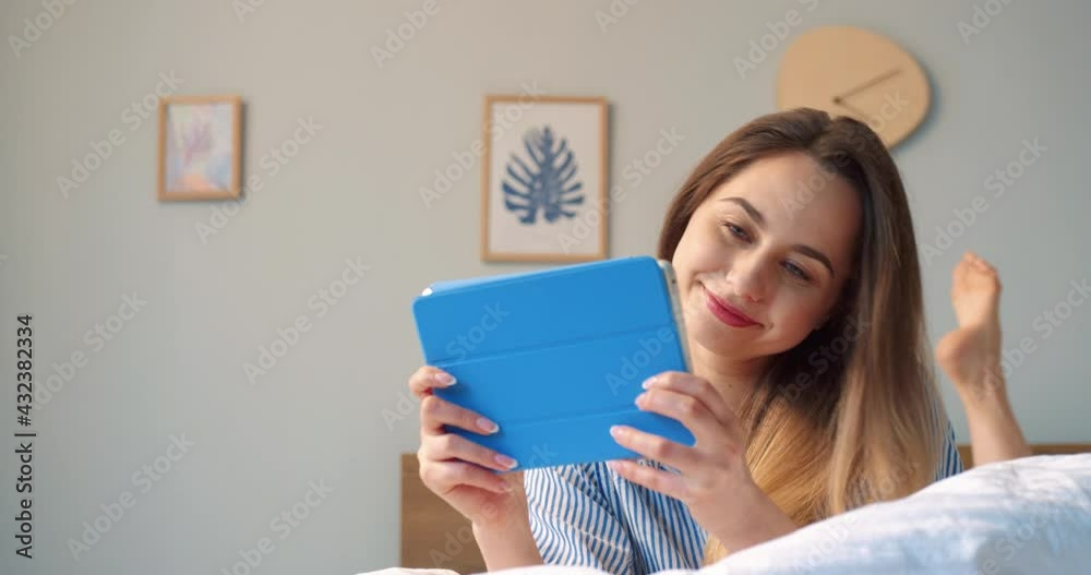 Portrait view of the pleasant blonde woman laying with tablet at the bed and having video call with friends or family. Cheerful woman smiling and speaking with good emotions Portrait view of the pleasant blonde woman laying with tablet at the bed and having video call with friends or family. Cheerful woman smiling and speaking with good emotions