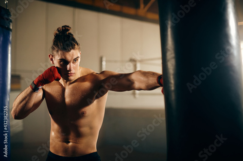 Muscular build fighter hitting punching bag while exercising in a gym.