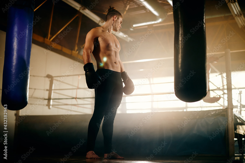 Full length of young boxer in front of punching bag at boxing club.
