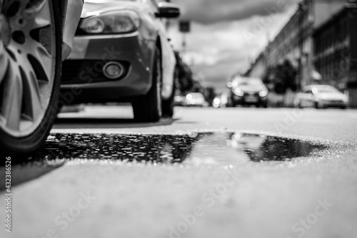 Sunny day after rain in the city, the headlights of the approaching car. Close up view of a wheel of a car parked in a puddle level