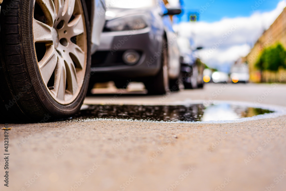 Sunny day after rain in the city, the headlights of the approaching cars. Close up view of a wheel of a car parked in a puddle level Sunny day after rain in the city, the headlights of the approaching cars. Close up view of a wheel of a car parked in a puddle level