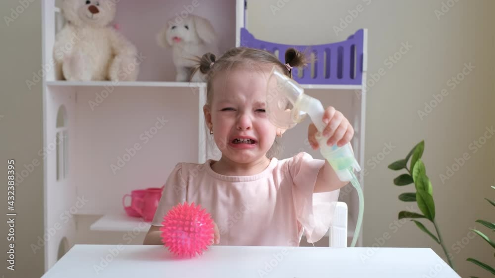A little girl cries while Inhalations. Children's diseases. Inhalations for runny nose, respiratory diseases and allergies. Children's nebulizer for inhalation. The child holds a breathing mask A little girl cries while Inhalations. Children's diseases. Inhalations for runny nose, respiratory diseases and allergies. Children's nebulizer for inhalation. The child holds a breathing mask