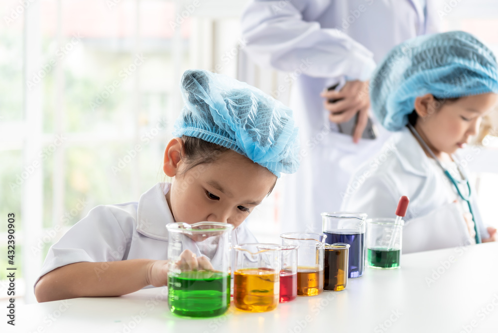 A 4 year old Asian girl, Learning And conducted a scientific experiment on a white table with a measuring cup, with blur her friend background, to children and education concept. A 4 year old Asian girl, Learning And conducted a scientific experiment on a white table with a measuring cup, with blur her friend background, to children and education concept.