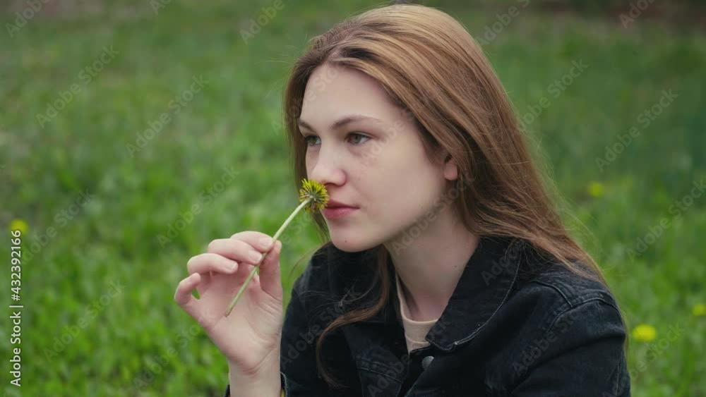 Beautiful young woman on a field with green grass and yellow dandelion flowers in a sunny day. Young woman sniffing yellow dandelion flower. Slow motion. Beautiful young woman on a field with green grass and yellow dandelion flowers in a sunny day. Young woman sniffing yellow dandelion flower. Slow motion.