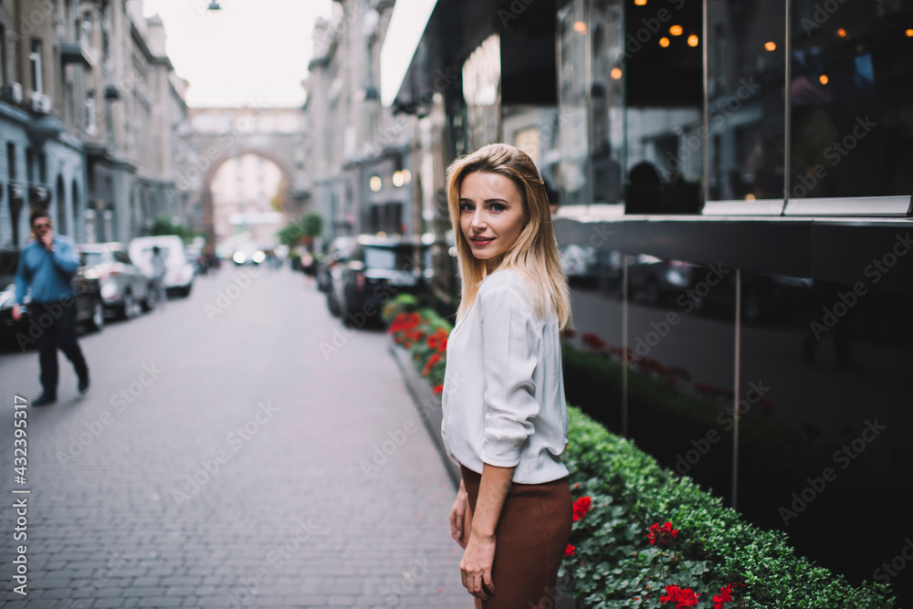 Fototapeta premium Young woman beside modern building on street in evening