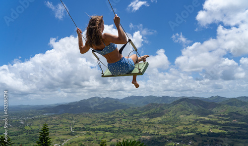 Young woman on the rope swing with sky and mountains background. Concept of freedom and happiness 