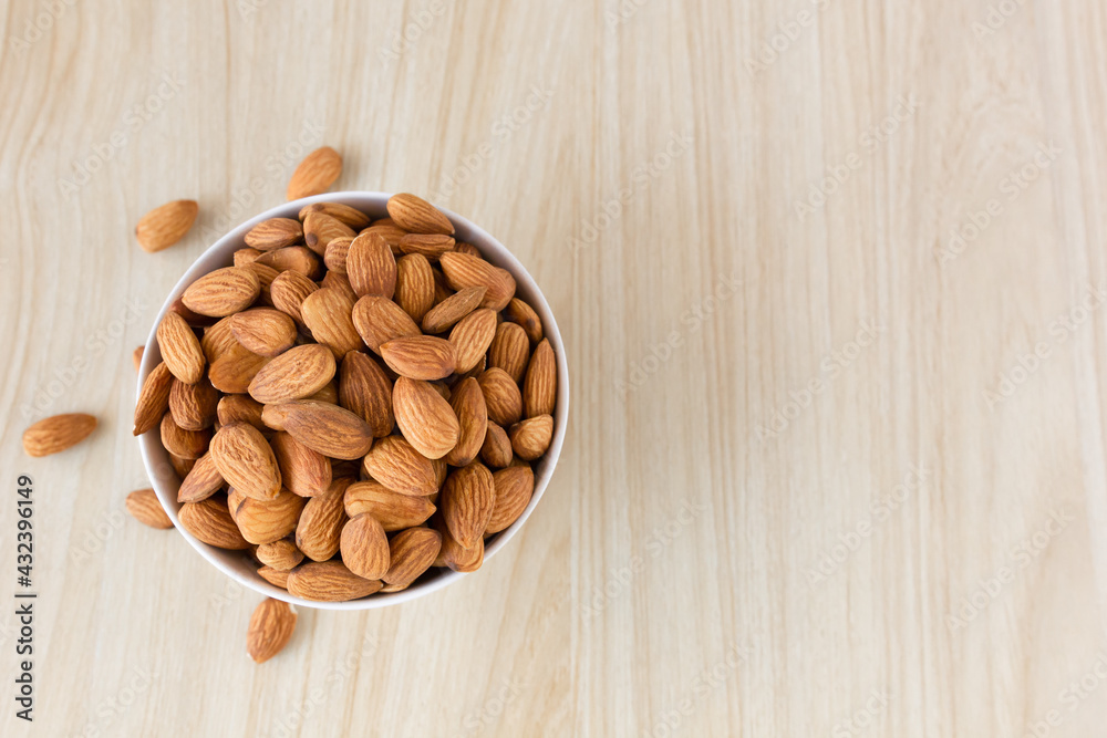 Almond nuts in a white bowl on wooden background, top view, flat lay, top-down, selective focus.copy space. Almond nuts in a white bowl on wooden background, top view, flat lay, top-down, selective focus.copy space.