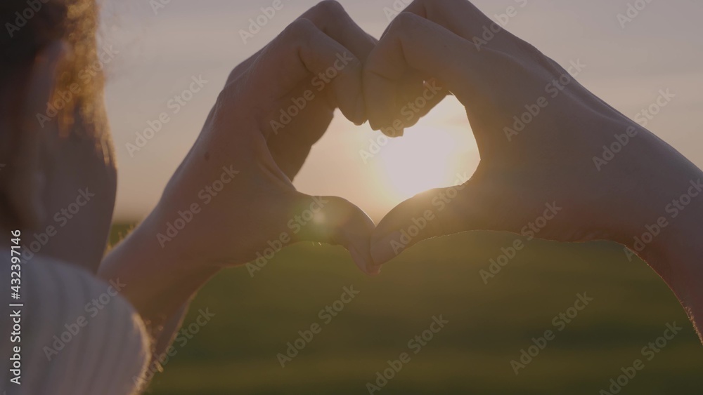Portrait of a girl from the hands made a heart shape at sunset, against an orange background. Concept: love to relax , freedom, love, life style, evening sunset, summer, sun.
