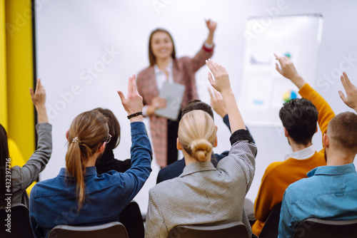 Fotografie Group of young people sitting at a conference together raised hands to express their views