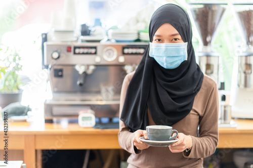 Beautiful Muslim woman, cafe owner or clerk We are preparing to serve coffee to customers in the shop with a backdrop of equipment and coffee machines.focus on cup