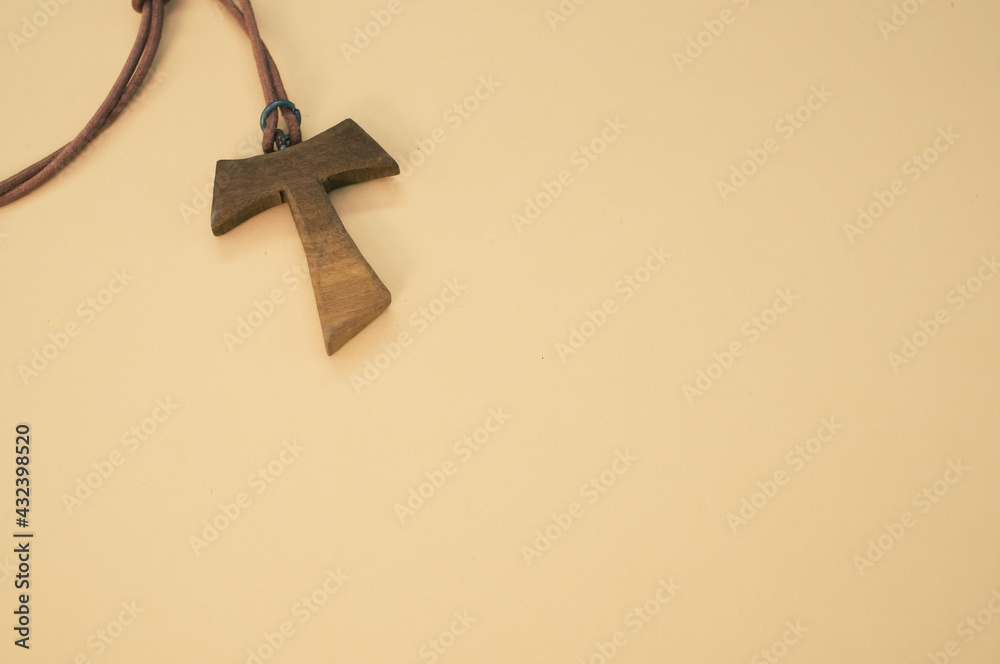 Closeup shot of a wooden tau cross necklace isolated on a brown background - obrazy, fototapety, plakaty 
