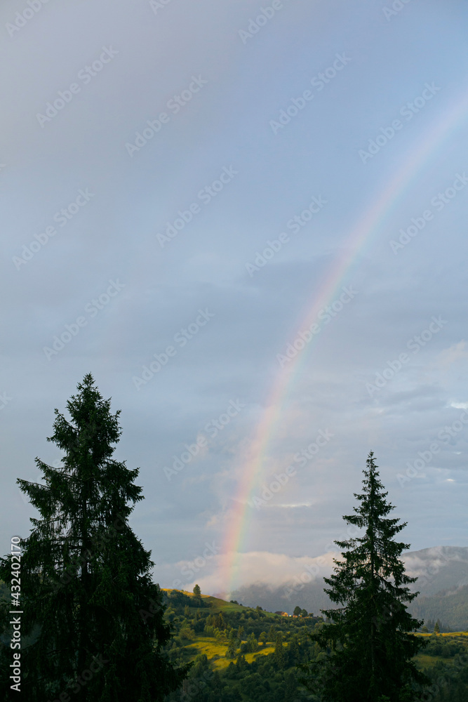 Rainbow in mountains after rain. Beautiful view on mountain hill with rainbow from cloudy sunny sky Rainbow in mountains after rain. Beautiful view on mountain hill with rainbow from cloudy sunny sky