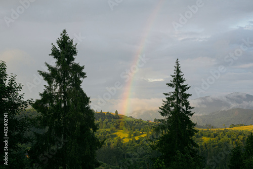 Rainbow in mountains after rain. Beautiful view on mountain hill with rainbow from cloudy sunny sky