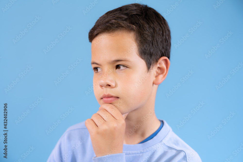 Beautiful young boy wearing blue sweater very pensive over blue background Beautiful young boy wearing blue sweater very pensive over blue background