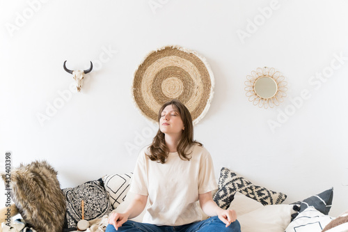 A healthy lifestyle. A woman rests in casual clothes in an authentic room. Lotus pose on the sofa, meditation