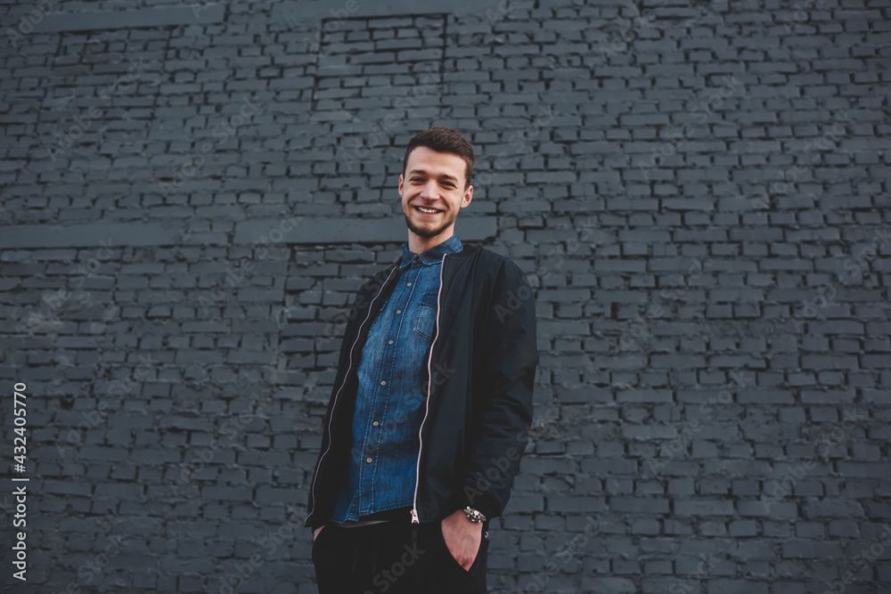 Positive young man standing near brick wall on street Positive young man standing near brick wall on street