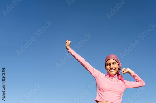 Young woman with cancer with gestures of victory and joy in the face of the disease. Celestial background and copy space. Hope, Struggle, Empowerment Concept.