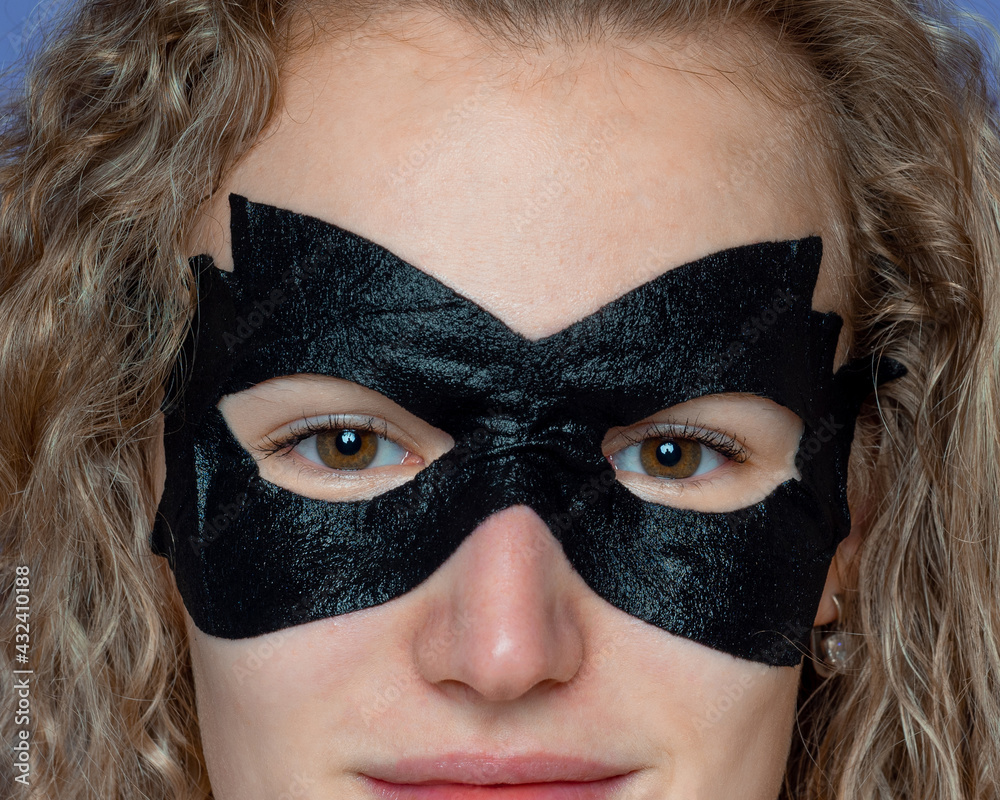 smiling girl with curly hair, in a black cosmetic mask for skin care and cleansing